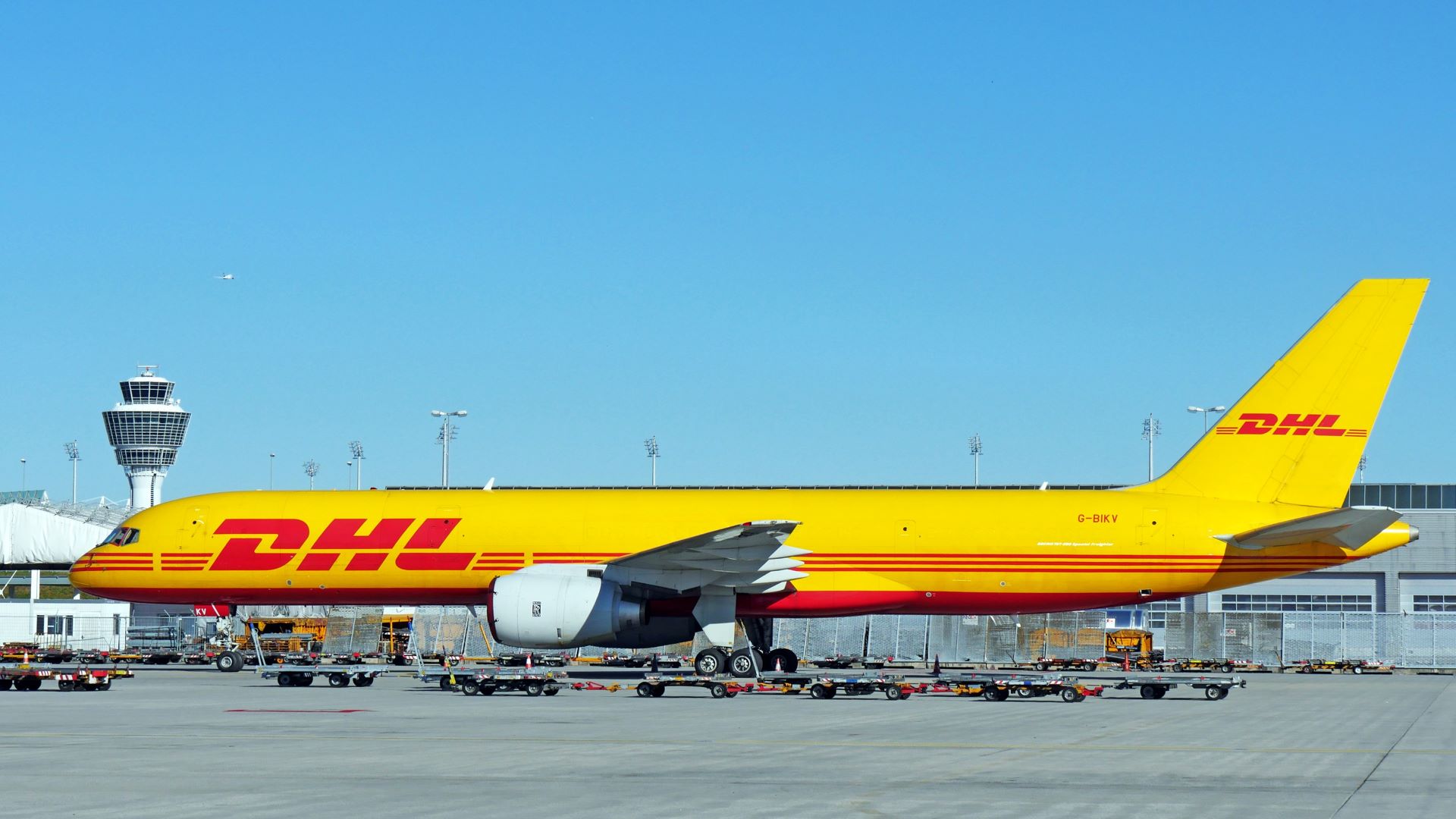 A mustard-yellow DHL plane on the tarmac on sunny day.