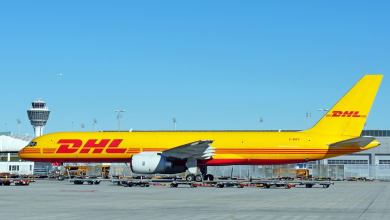 A mustard-yellow DHL plane on the tarmac on sunny day.