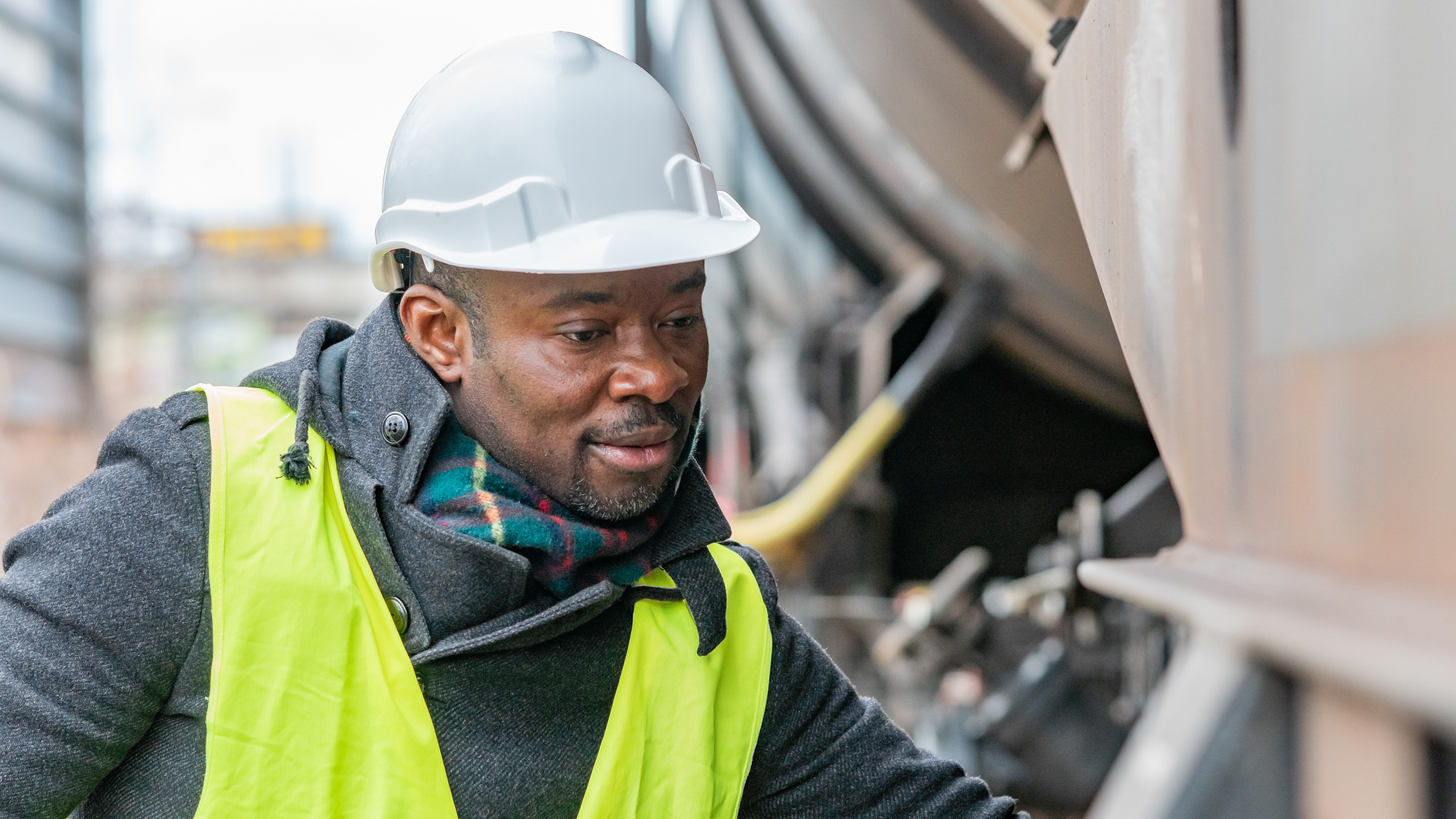 An man wearing a hard hat and a neon work vest looks closely at a railcar.