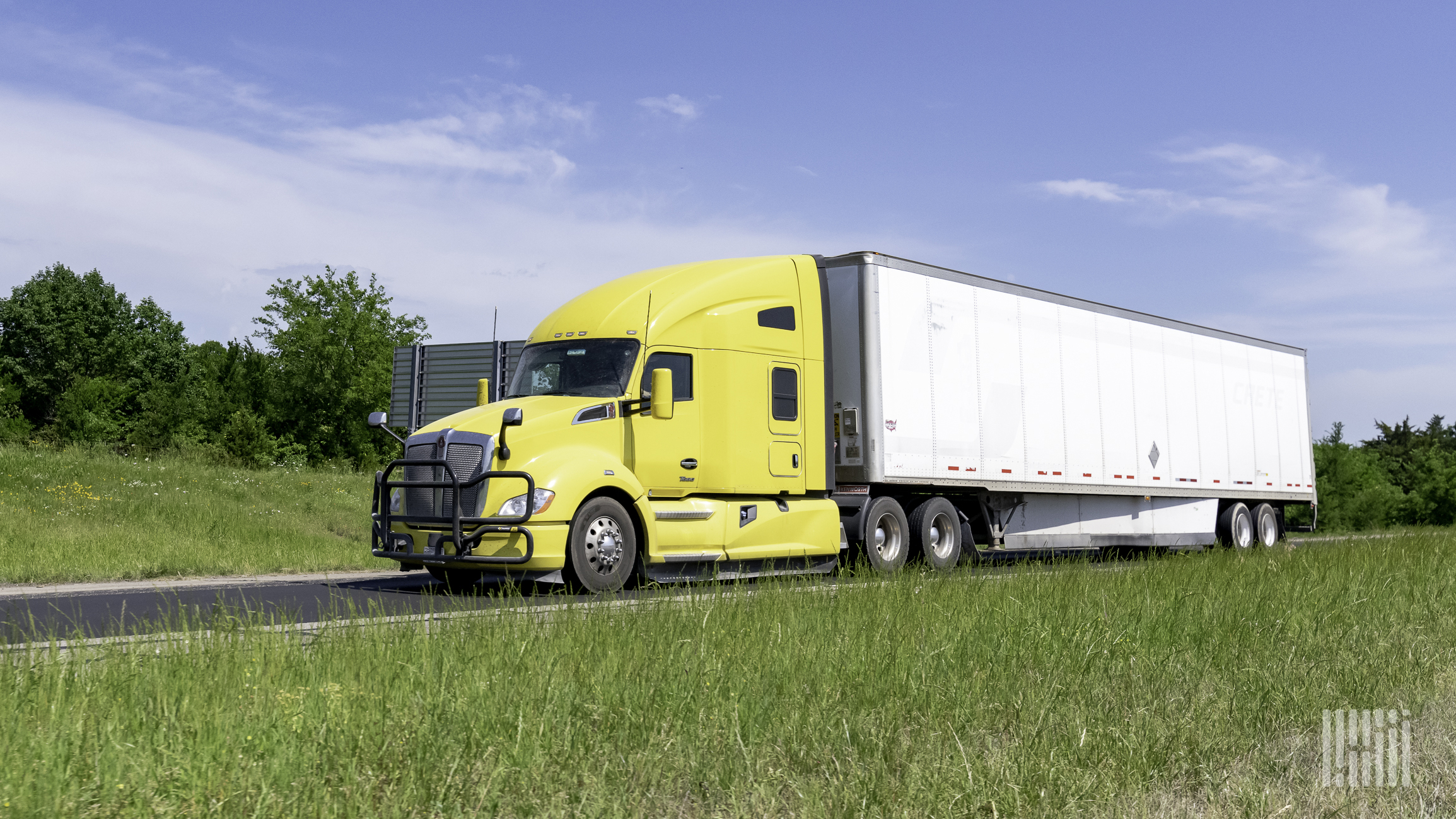 A yellow tractor pulling a white trailer on highway