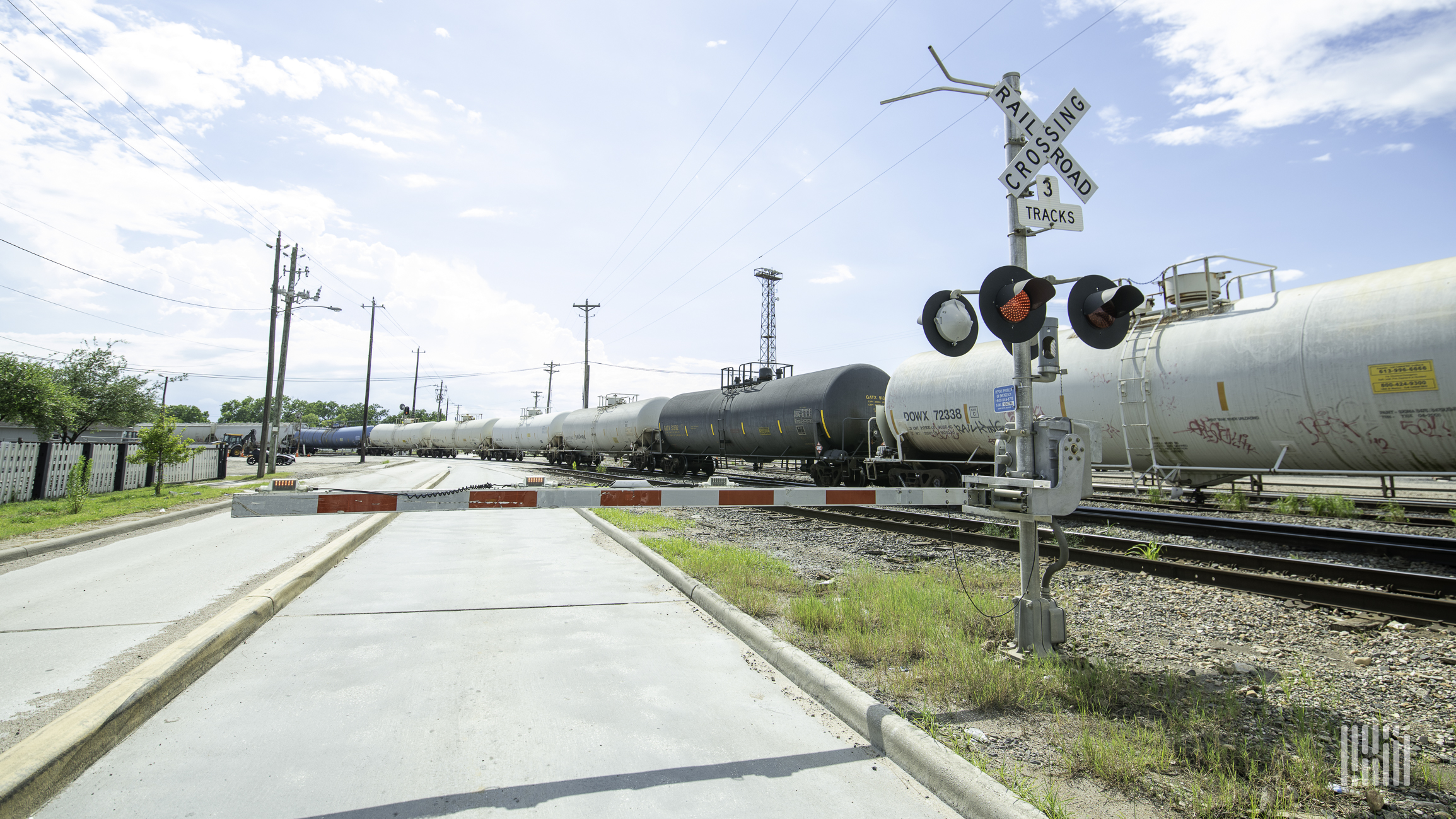 A train of tank cars passes by a railroad crossing