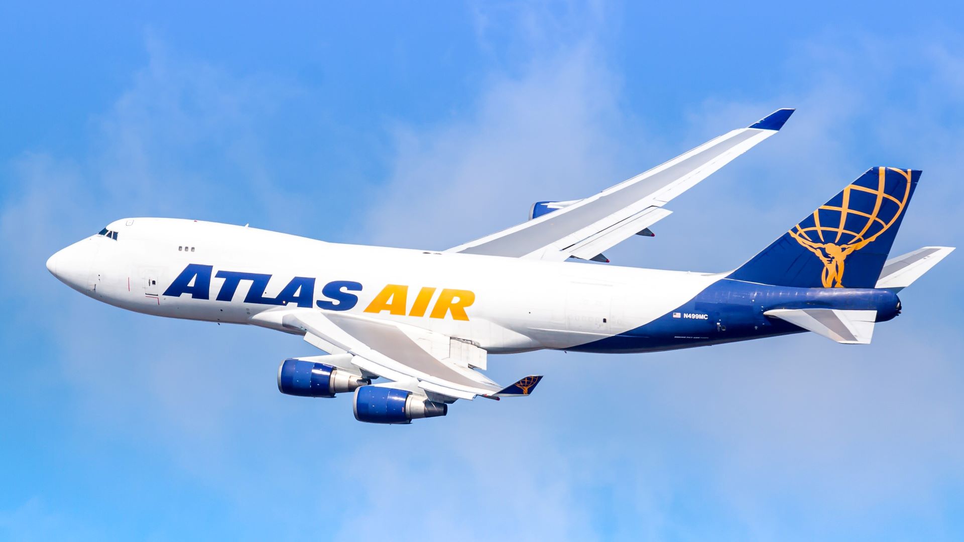 A white Atlas Air jumbo jet with blue tail, and gold lettering flies in blue sky.
