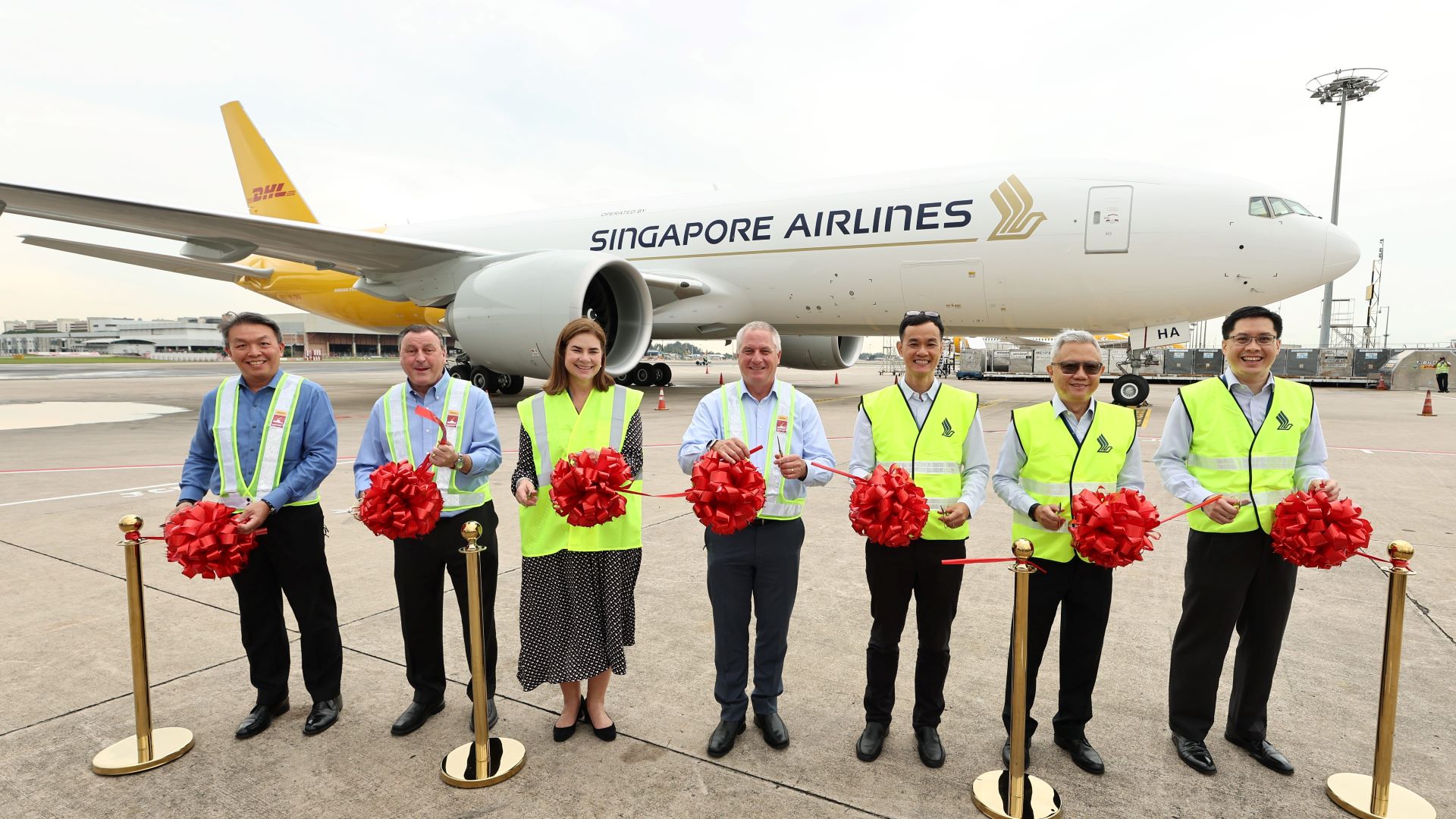 Singapore Airline workers stand with bows in front of new cargo jet with Singapore and DHL logos.