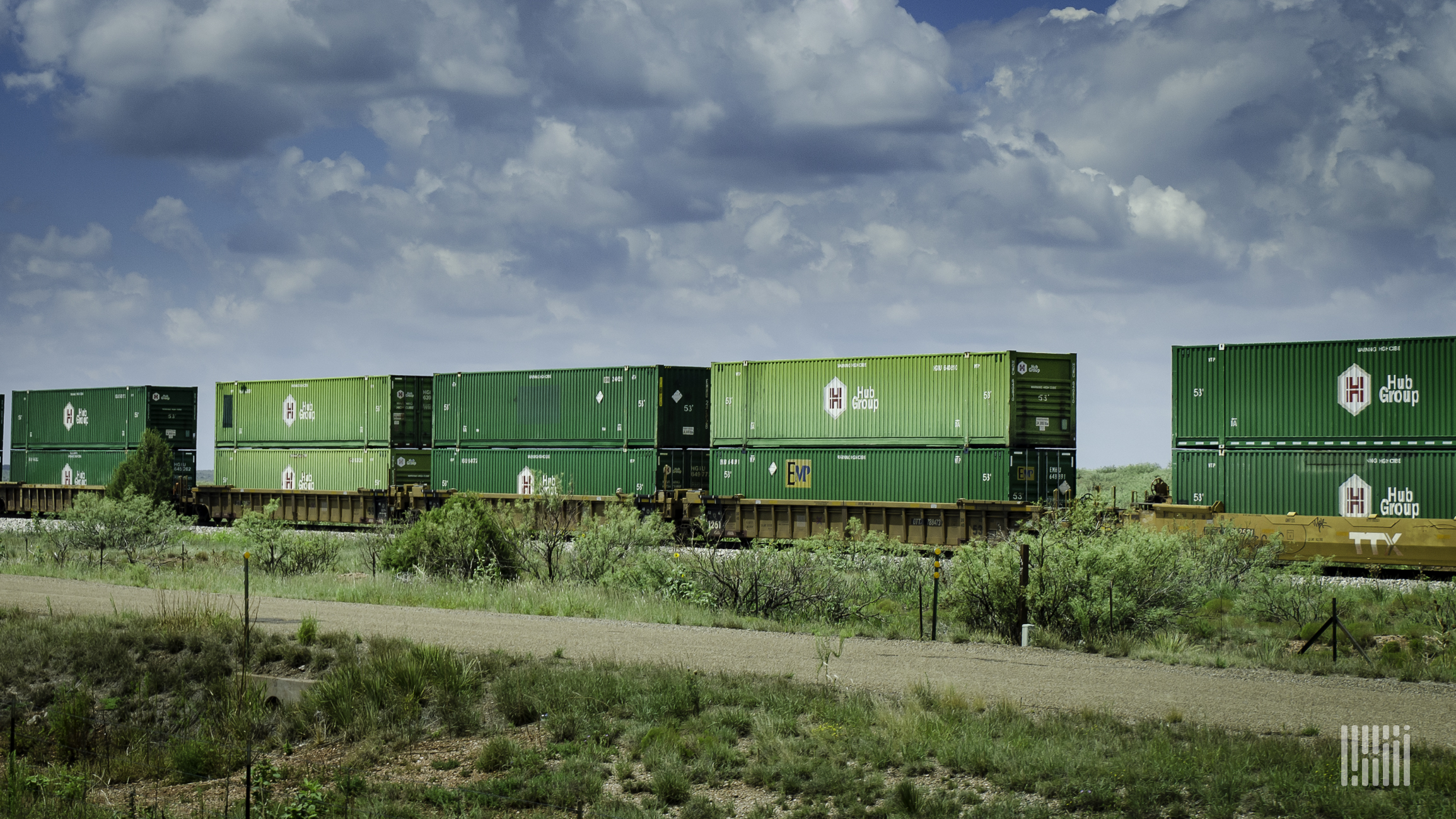 Double-stacked containers sit on a train that is passing through a grassy field.