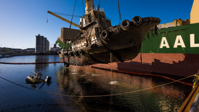 A mud-covered tugboat being lifted by cranes from a salvage vessel.