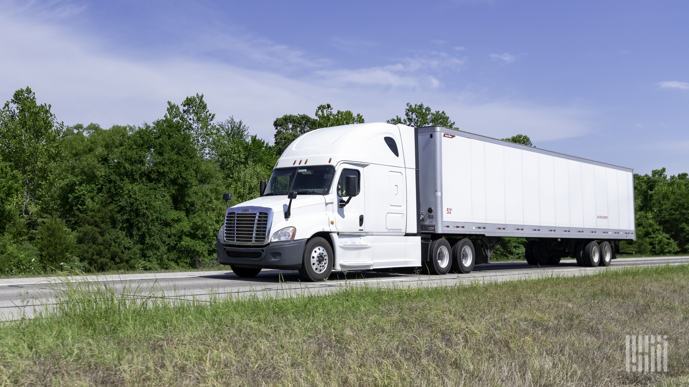 A white tractor pulling a white trailer on the highway