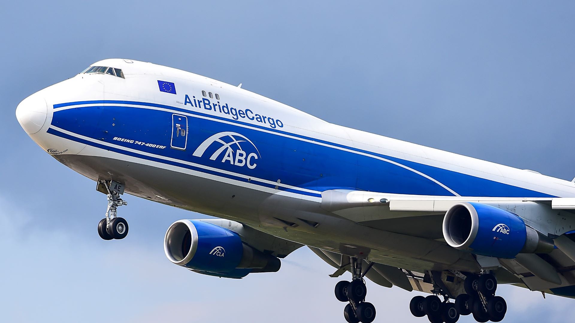 A close up view of a blue-white AirBridgeCargo jumbo jet with wheels down on approach to airport.