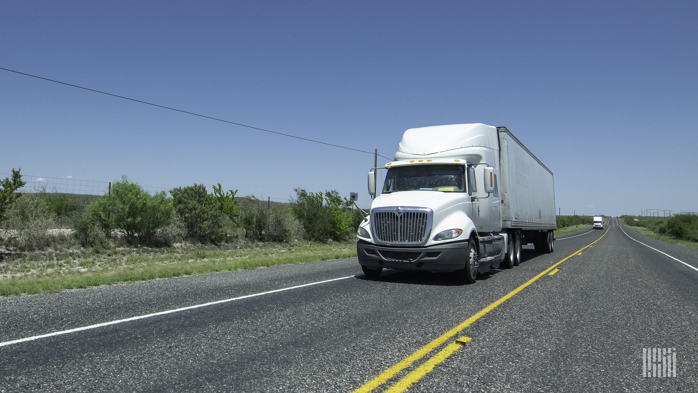 A white tractor pulling a trailer on the highway