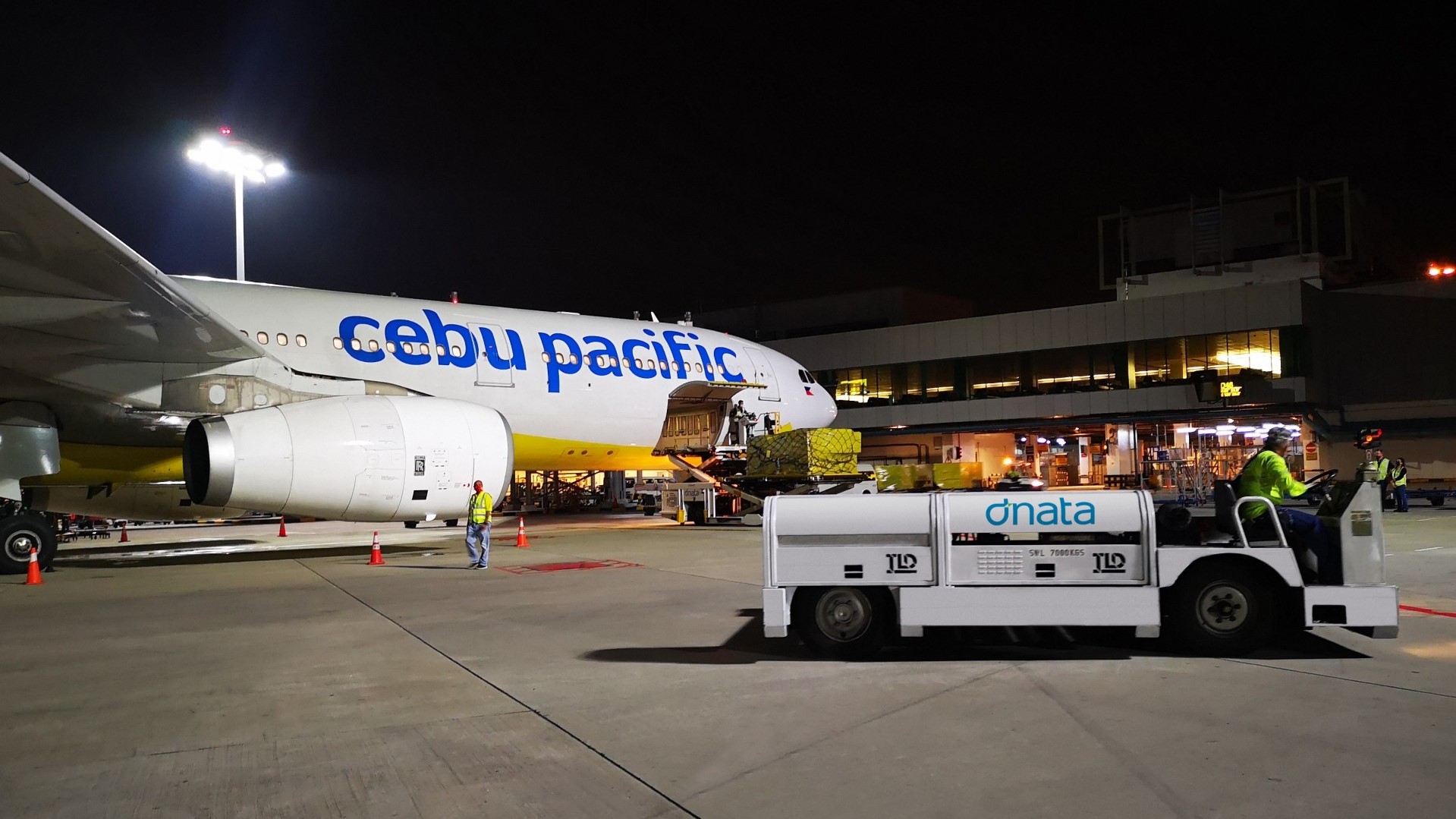 A Cebu Pacific jet being loaded with cargo at night while an airport tug drives by.