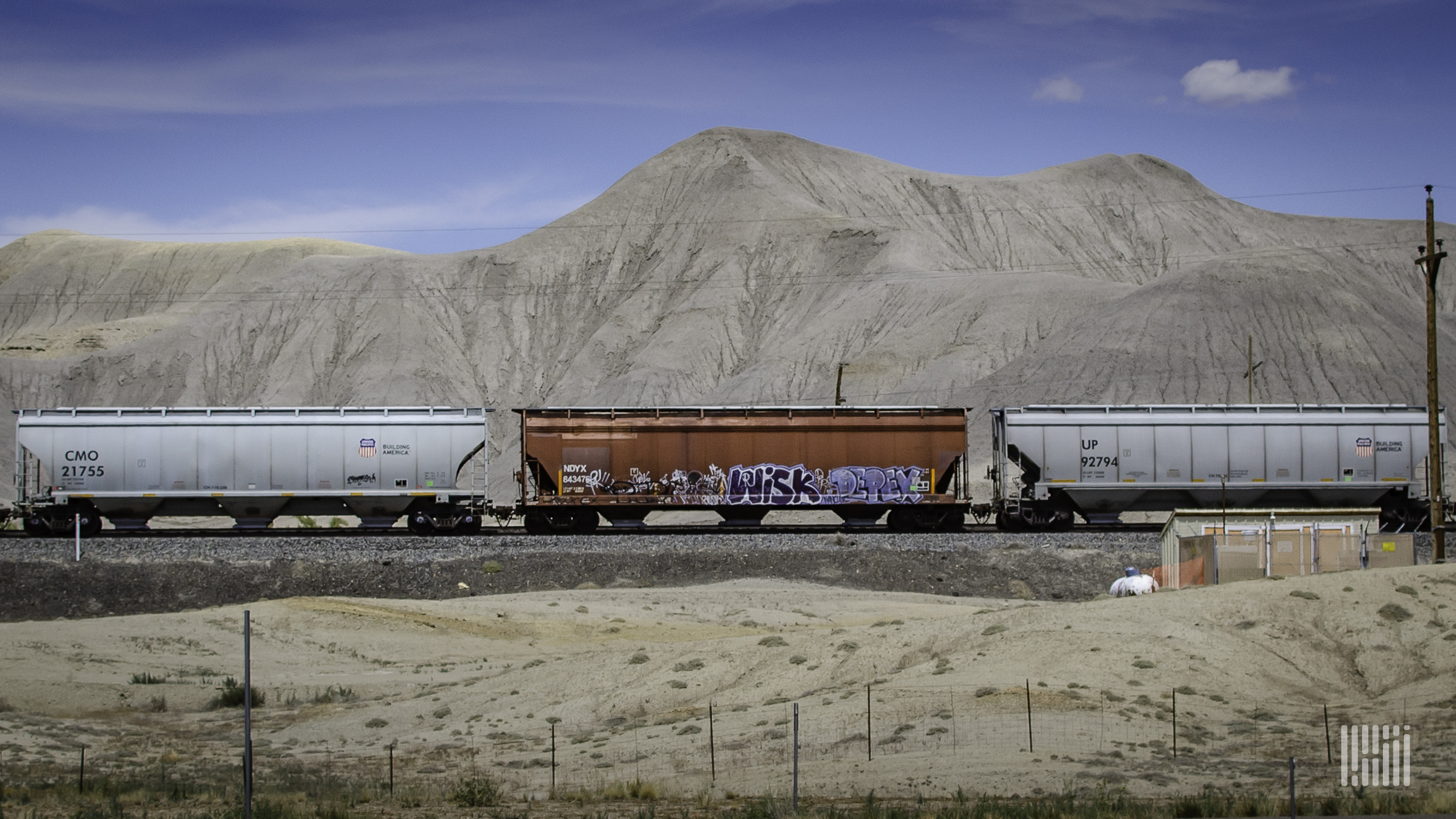 A train hauling hopper cars passes through a desert.