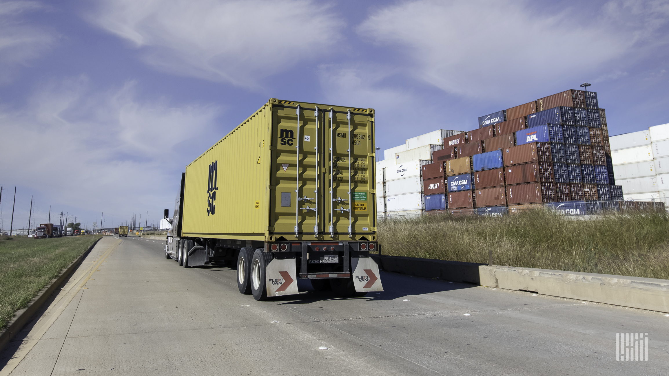 A yellow ocean container being pulled by a truck