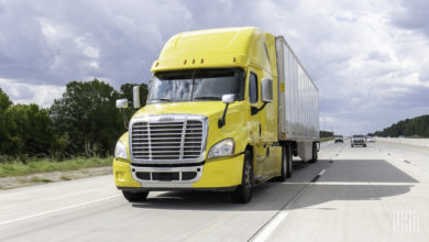 A yellow tractor pulling a white trailer on the highway