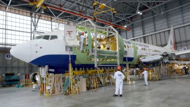 A white plane with blue bottom on a stand in hangar getting repaired.