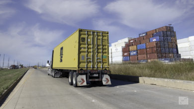 A tractor pulling a chassis with a yellow container at a port