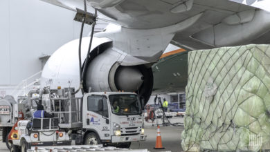 A cargo pallet and a fuel truck under the wing of a large jet.