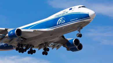 A blue-and-white jumbo jet for cargo comes in for landing against blue sky, looking up at plane.