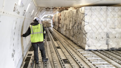 A man with a yellow vest inside the cargo bay of a large jet with large containers on the floor.