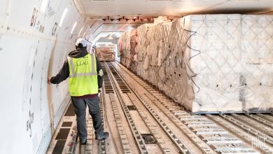 A man with a yellow vest inside the cargo bay of a large jet with large containers on the floor.