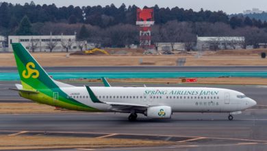 A white jet with light-green tail and Spring Airlines Japan written on fuselage rolls across airport road.