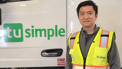 TuSimple CEO Cheng Lu standing in front of a truck's door with company name.