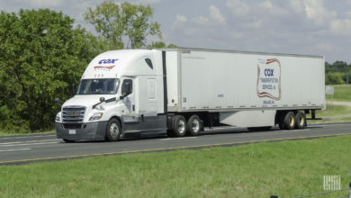 A white Cox tractor pulling a white Cox trailer.