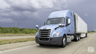 A light blue tractor pulling a silver trailer on the highway