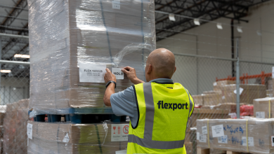Picture from behind a man in a yellow vest with Flexport label working in a warehouse.