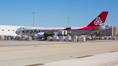 A white Cargolux jumbo jet with red tail parked next to a warehouse on a sunny day.