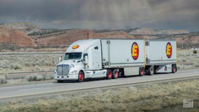 A white Estes tractor pulling two Estes LTL trailers on a highway .