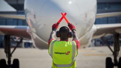 A ramp worker with a yellow jacket signals to the pilot in an aircraft.