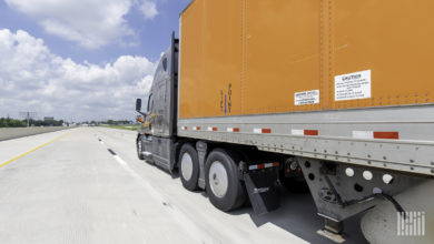 A gray Schneider tractor pulling an orange trailer on the highway