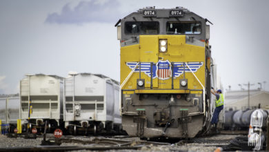 A Union Pacific train is parked in a rail yard next to some hopper rail cars.