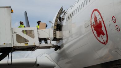 Workers on an elevated platform unload boxes from a jet with the Air Canada logo.