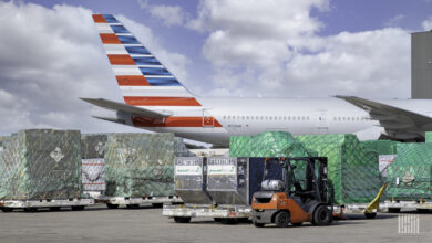 Cargo pallets with green shrink wrap sit by an a jet with an American flag them painted on tail.