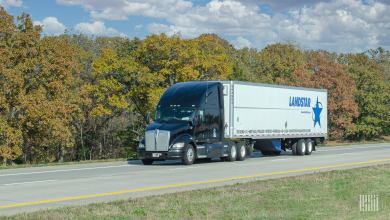 A black tractor pulling a white Landstar trailer on the highway