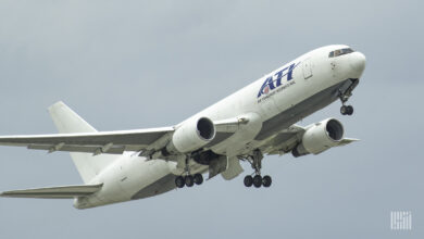 A white jet with ATI logo in the air after takeoff with wheels down.
