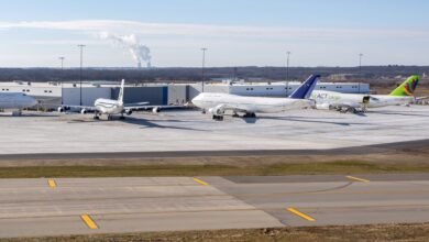 Several large planes parked next to a cargo warehouse at an airport on a sunny day.