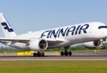 A white jet with blue Finnair lettering touches down on runway on sunny day.