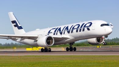 A white jet with blue Finnair lettering touches down on runway on sunny day.