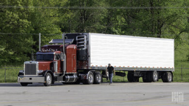 A driver walks along the side of a parked semi truck