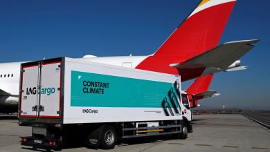 A box van with IAG Cargo lettering and green banner "Constant Climate" on the side in front of a large jet with a red tail.