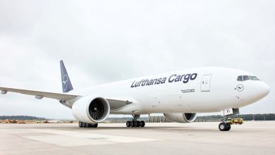 A white jet with blue tail and lettering "Lufthansa Cargo" on the tarmac, viewed from side ground level.