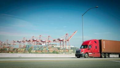 A red truck pulls an ocean container near a port