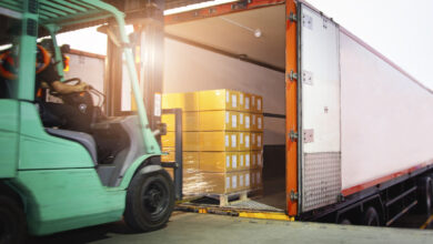 Forklift Driver Loading Package Boxes into Cargo Container. Cargo Trailer Truck Parked Loading at Dock Warehouse. Shipment Delivery Service. Shipping Warehouse Logistics. Freight Truck Transportation.