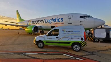 A van parked in front of a cargo jet, both in white and lime green colors of Modern Logistics as dawn sun creeps up.