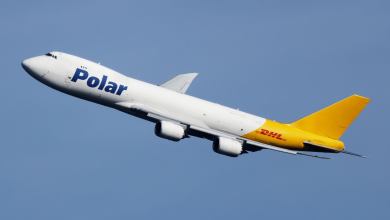 A white jumbo jet, painted two-thirds white and one-third mustard yellow, with a blue Polar logo angles up through the sky.
