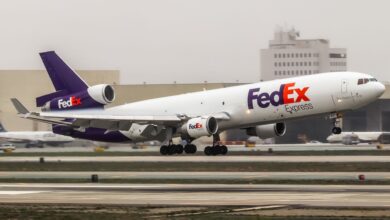 A purple-tail FedEx plane lifts off from a runway on a cloudy day.