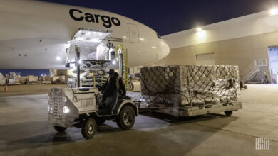 An airport driver pulls a cargo pallet next to a large cargo jet at night.