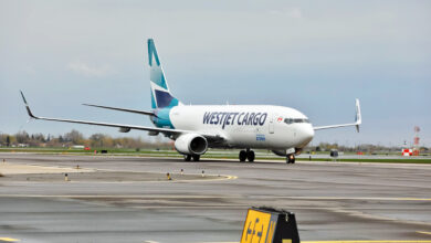 A teal-tailed WestJet Cargo plane rolls on the runway on a gray day.