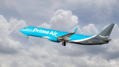 A light blue Amazon Prime Air jet takes off into cloudy sky on bright day.